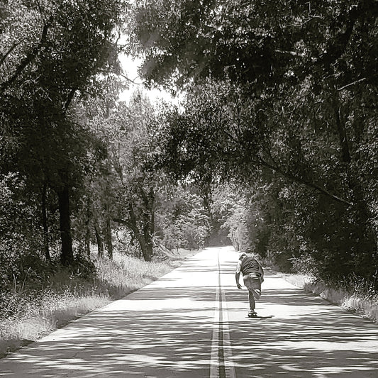 Black and white picture of a skateboarder skating down a lonely country highway